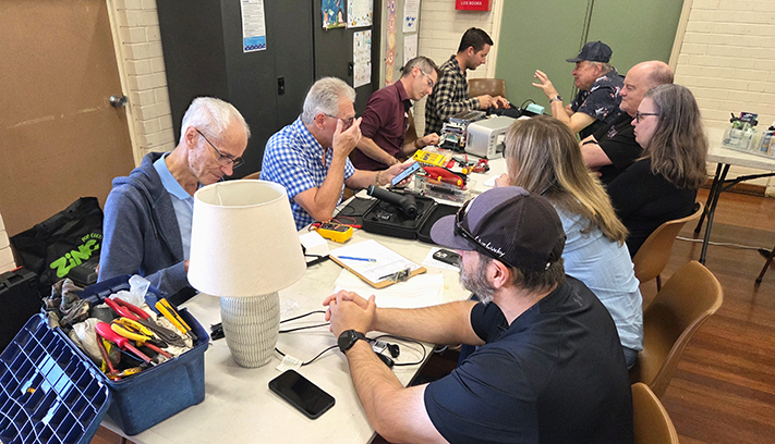 A group of people repair household objects around a table.