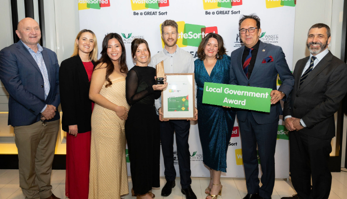 A group of smiling people stand together after receiving an award,.