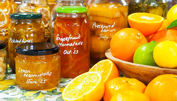 Jars of homemade marmalade and preserved citrus displayed alongside fresh oranges, lemons and limes.