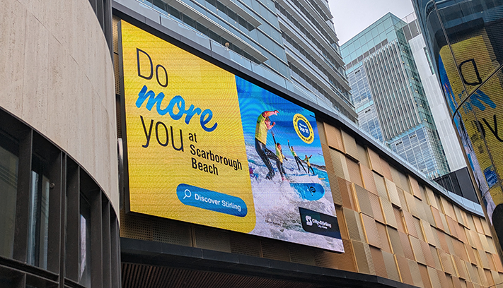 Large digital billboard promoting Scarborough Beach on the side of a city building, featuring surfers and City of Stirling branding.