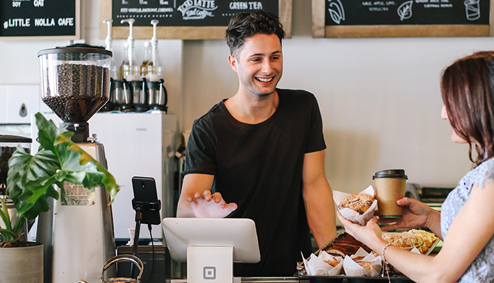 ustomer purchasing coffee and pastries at a local café counter, with menu boards and coffee equipment in the background.