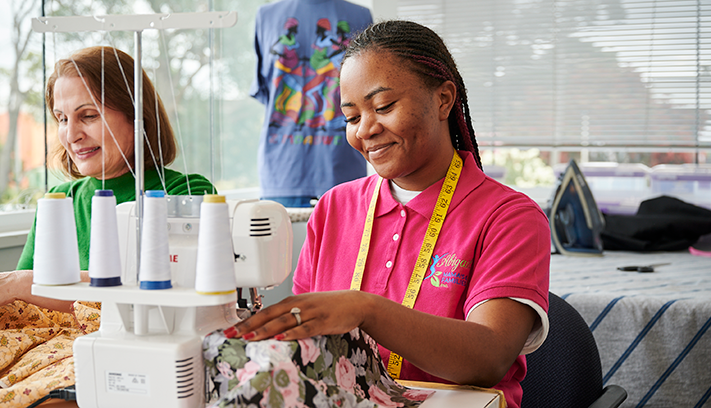 Participants gathered around sewing machines during a clothing repair and sewing workshop, with one person demonstrating fabric stitching.