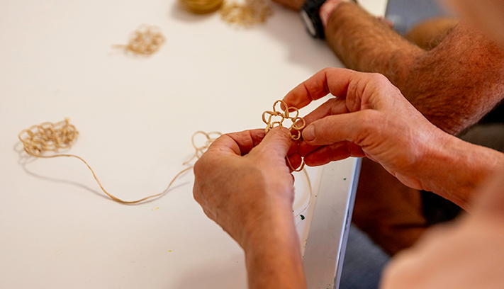 Close-up of hands weaving thin strands into a small handcrafted pattern during an arts and crafts workshop.