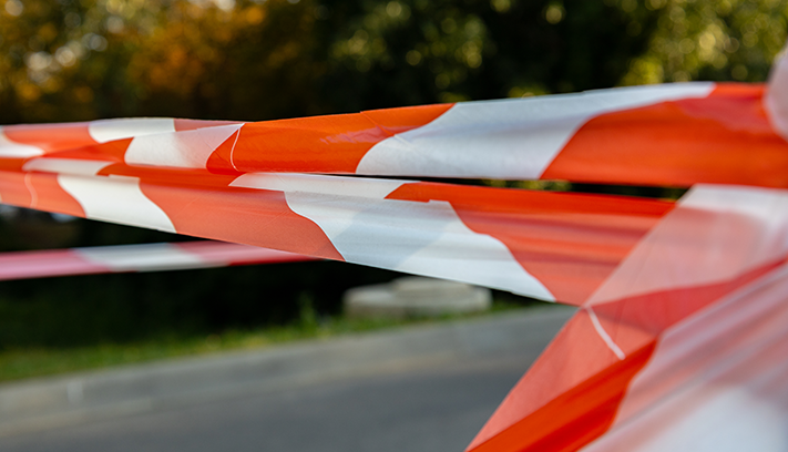 Caution tape across a road with bush in the background.