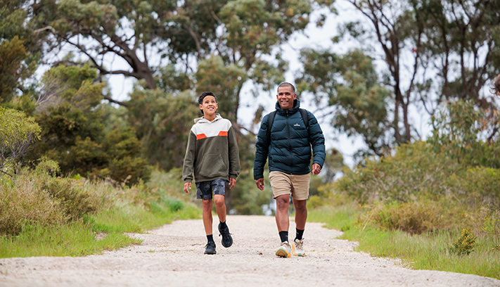 A father and son walk along a broken path in urban bushland.