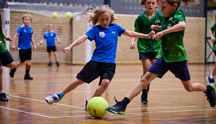 A young soccer player kicks a ball in a gymnasium.