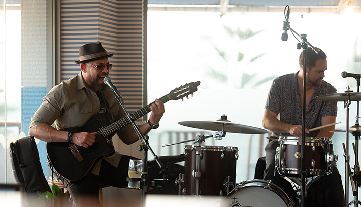A jazz performer sings and plays guitar with a drummer.