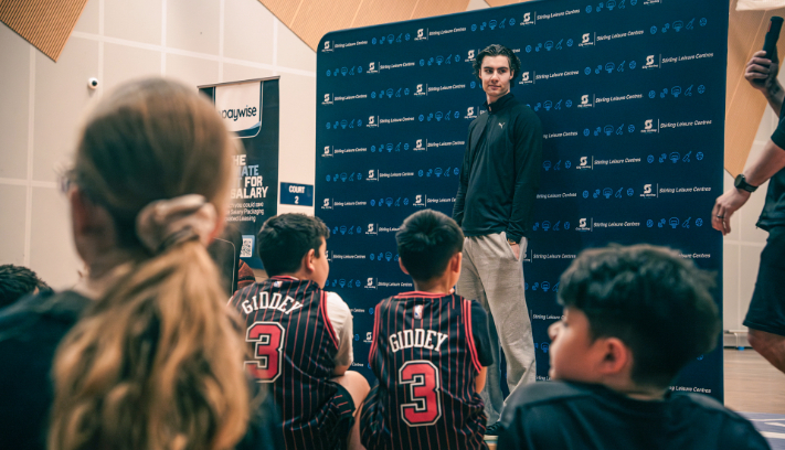 A basketball player stands in front of a group of children.