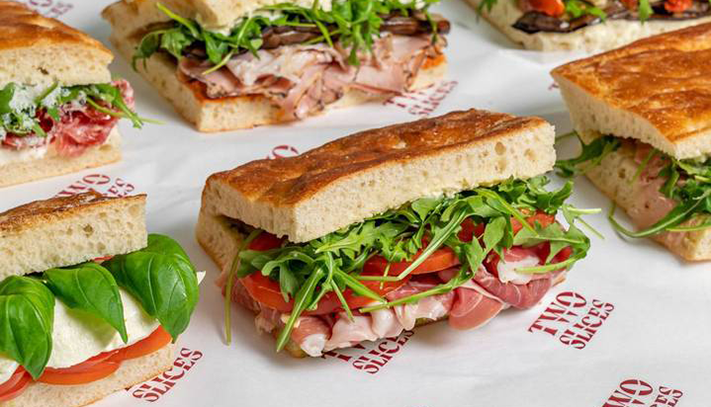 Assorted gourmet sandwiches and focaccias filled with cured meats, cheese, tomato and fresh salad greens, displayed on a catering table.