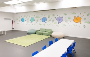 Children’s activity room with tables, soft seating and a colourful monster mural painted across one wall.
