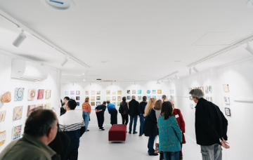 Visitors viewing and discussing artwork displayed throughout a gallery exhibition space.