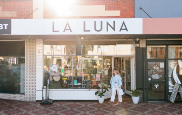 Person walking past the La Luna storefront on a local shopping strip, with shopfront displays and signage visible.