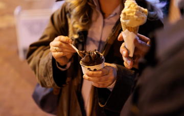 People enjoying gelato and ice cream cones while strolling along a street at night.