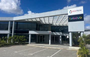 Modern commercial office building with glass façades and prominent VeinTech and Lubdub signage above the main entrance, viewed from a car park on a clear day.