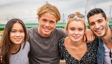 Four young people standing together outdoors, posing for a group photo in an urban setting.