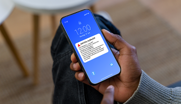Person holding a smartphone displaying a critical emergency alert notification on the lock screen.