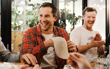 People seated around a table during a social dining event, preparing food together and chatting in a restaurant setting.