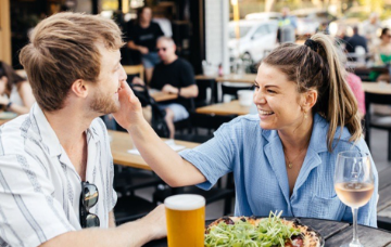 Two people dining at an outdoor café table, sharing a meal and drinks in a lively restaurant setting.