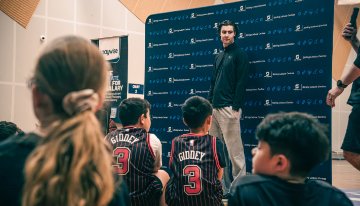 A basketball player stands in front of a group of children.