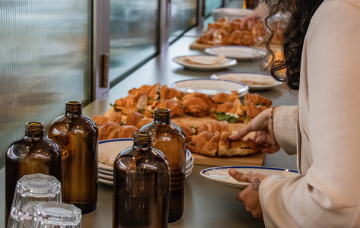 Person selecting a pastry from a catering table with croissants, plates and glassware at a business networking event.